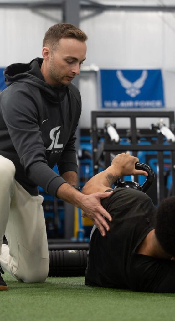 Rehab Lab provider guiding a patient through a corrective exercise movement with a kettlebell in a gym setting.