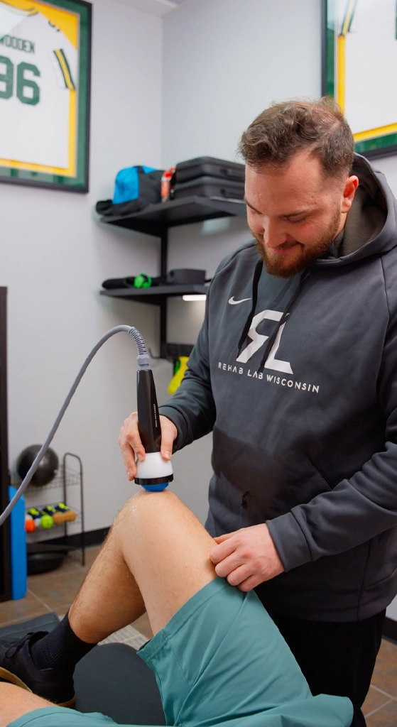 Provider at Rehab Lab Wisconsin performing a StemWave treatment on a patient’s knee in a therapy room.